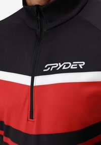 Giacca a zip rossa e nera con colletto alto, strisce orizzontali di nero, bianco e rosso, e un logo "SPYDER" ben visibile.