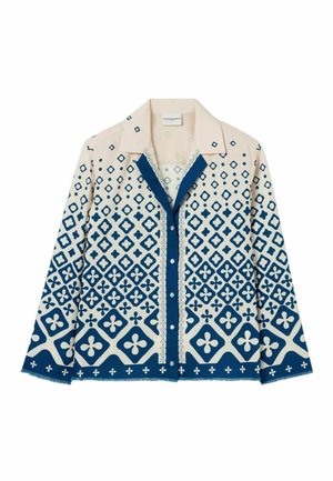 Camisa de botones con una base en color crema y patrones geométricos azules, incluyendo diamantes y motivos florales, y un cuello en contraste.