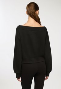 Felpa nera con scollatura a spalle scoperte, maniche lunghe a palloncino e vita aderente. Tessuto liscio con dettagli di cucitura minimi.