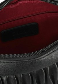 Interiores de un bolso de mano de cuero negro con forro de tela roja, que presenta un cierre de cremallera y un pequeño bolsillo con cremallera en un lado. Diseño de superficie texturizada.