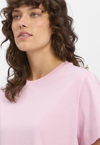 Hellrosa Baumwoll-T-Shirt mit Rundhalsausschnitt und kurzen Ärmeln, das eine glatte Textur und ein minimalistisches Design aufweist.