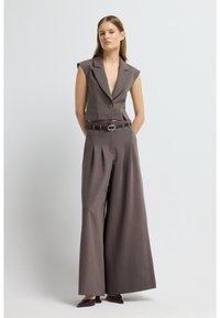 Šedá oříznutá vesta s výřezem na límci a jedním knoflíkem, doplněná širokými kalhotami s plisováním a odpovídajícím opaskem.
