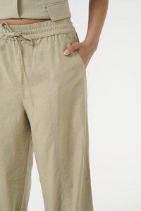 Pantaloni elasticizzati color beige chiaro con vita alta e coulisse, dotati di tasche laterali e realizzati in un tessuto liscio e texturizzato.