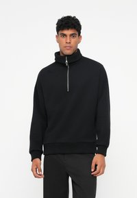 Zwarte zip-up sweatshirt met hoge kraag. Beschikt over een ritssluiting aan de voorkant en lange mouwen met geribbelde manchetten en zoom. Gemaakt van zachte stof.
