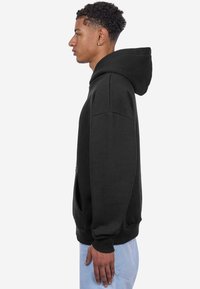Sweatshirt à capuche noir avec une coupe décontractée, fabriqué en tissu doux. Dispose de poches latérales et de poignets côtelés. Vue de profil.