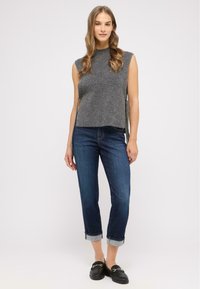 Top grigio senza maniche in maglia con colletto alto, abbinato a jeans blu scuro con risvolto. Mocassini neri completano l'outfit.