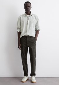 Light green and white striped button-up shirt paired with dark green trousers and white sneakers. Clothing features casual fits and pockets.