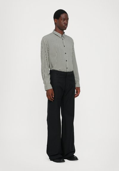 Chemise boutonnée à carreaux noirs et blancs avec col, portée avec un pantalon large noir et des chaussures noires. Tissu lisse et coupe structurée.