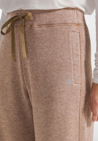 Bruine gebreide sweatpants hebben een gestructureerde afwerking, een olijfgroene trekkoord tailleband, zijzakken en een klein logo-detail op het been.