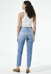 Lichtblauwe spijkerbroeken van denim met een hoge taille en een rechte pasvorm, voorzien van achterzakken en opgerolde zoom. Gecombineerd met een wit tanktop.