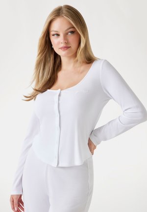 Witte geribbelde lange mouw top met een ronde halslijn, voorzien van een knoopsluiting aan de voorkant en subtiele geborduurde details op de borst.