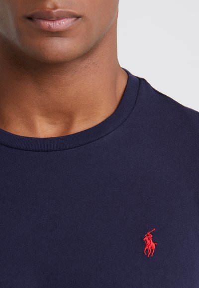 Navyblauwe katoenen T-shirt met ronde hals en een klein rood geborduurd ponylogo op de linkerkant van de borst, zachte textuur en korte mouwen.
