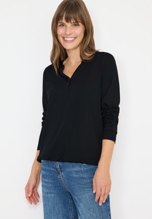 Top negro de manga larga con cuello tipo henley, que presenta tres botones y puños con fruncidos. Combinado con unos vaqueros azules. Textura suave.
