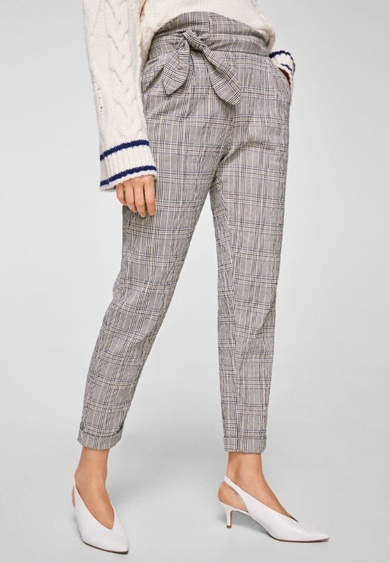 Spodnie w kratę z wysokim stanem w kolorze szarym, z detalem w postaci kokardy w talii, zwężanymi nogawkami i subtelnymi kieszeniami. W połączeniu z białymi butami na obcasie typu slingback.