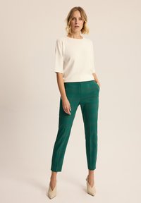 Biały krótki top z kwadratowym dekoltem, zestawiony z zielonymi, w kratkę spodniami w kroju garniturowym oraz beżowymi szpilkami z ostrym noskiem.