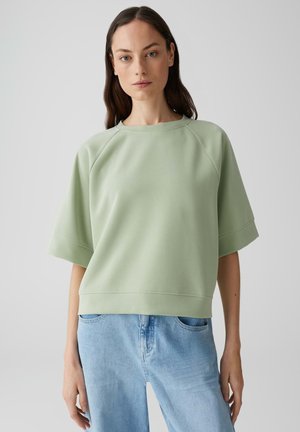 Lichtgroene oversized sweatshirts met een ronde hals, raglanmouwen en een gestructureerde afwerking, gecombineerd met lichtblauwe denim jeans.