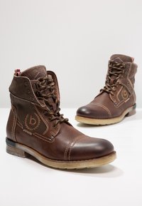 Botas de cuero marrón con puntera plana, diseño de cordones y acentos cosidos. Incluyen un suave cuello de tela y suela transparente.