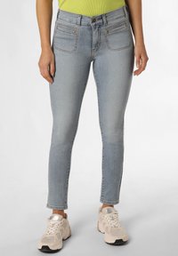 Jeans skinny de denim en un azul claro con cintura alta, bolsillos delanteros y dobladillo sin rematar. Combinados con zapatillas deportivas beige.
