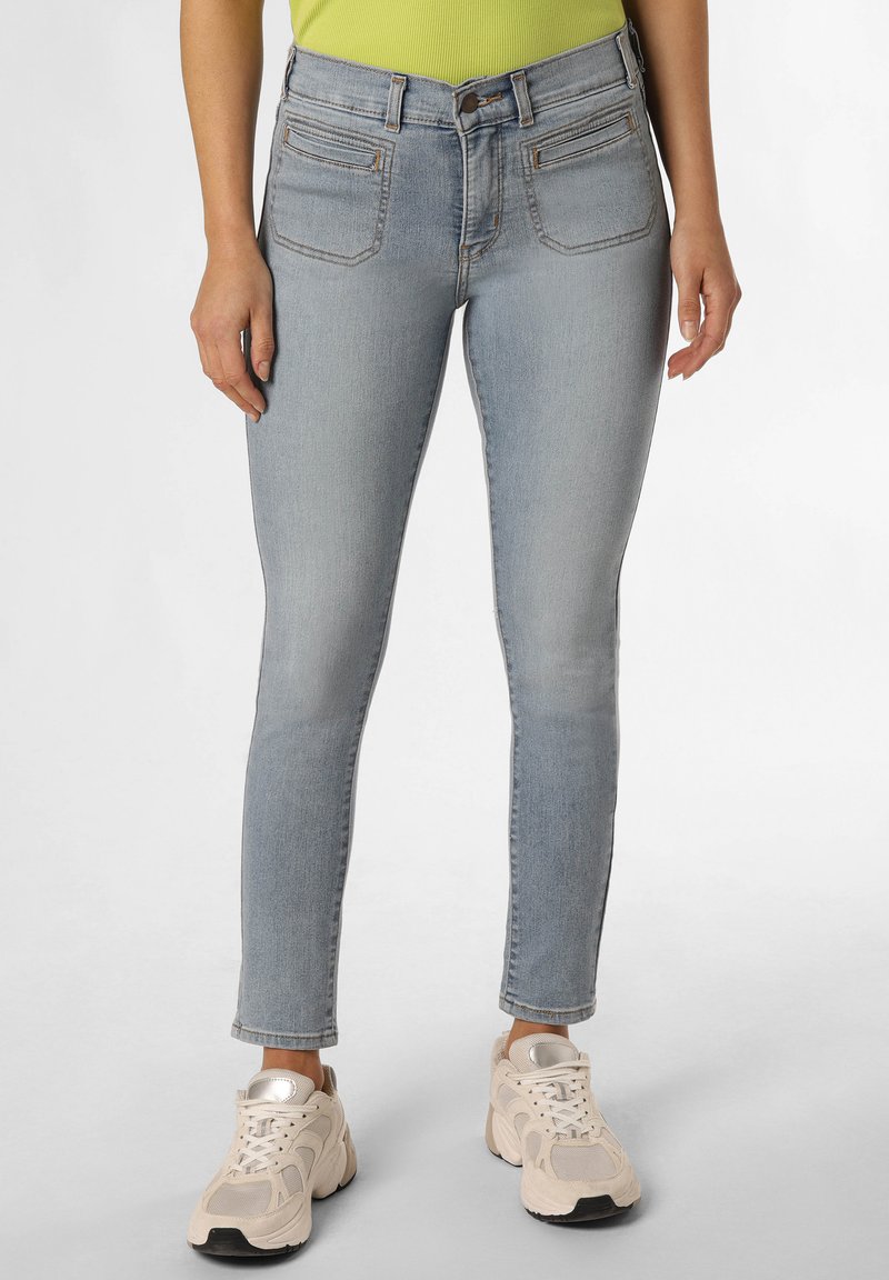 Jeans skinny de denim en un azul claro con cintura alta, bolsillos delanteros y dobladillo sin rematar. Combinados con zapatillas deportivas beige.