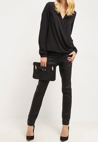 Blouse noire à manches longues avec un col en V, assortie à un pantalon noir slim et une pochette. Des talons complètent le look monochromatique et élégant.