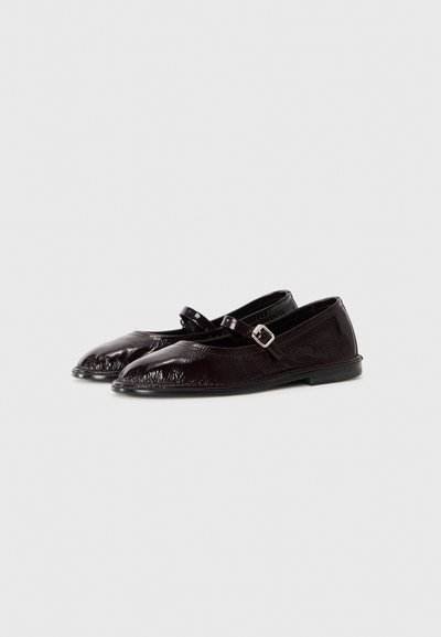 Chaussures Mary Jane en cuir verni noir avec une finition texturée, bout pointu et sangle réglable avec boucle en argent. Semelle plate.