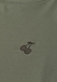 Cerises brodées brun foncé avec tiges sur fond en tissu vert olive, probablement partie d'un vêtement.