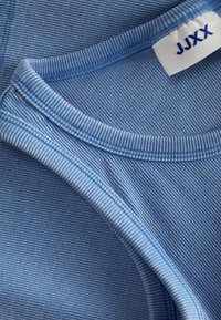 Camisola sem mangas azul clara com riscas horizontais, apresentando uma gola redonda e textura ribada. Rótulo visível com a marca "JJXX".