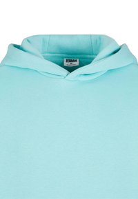 Svijetloplava hoodie izrađena od mekanog materijala. Ima klasičnu kapuljaču, rebraste manžete i oznaku koja indicira veličinu i brend "Urban Classics."