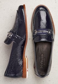 Navy patent leather loafers with a textured finish, silver hardware accent, and wooden heels combined with a white and red detail.