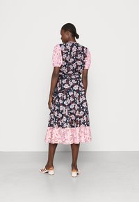 Vestido midi floral com uma base azul-marinho e padrões de flores cor-de-rosa, mangas bufantes e uma bainha rendada também cor-de-rosa. Usado com sandálias cor-de-rosa claras.