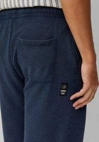 Navyblauwe joggingsbroek van een textuurstof met een elastische tailleband, voorzien van een patch pocket en een merketiket aan de zijkant.