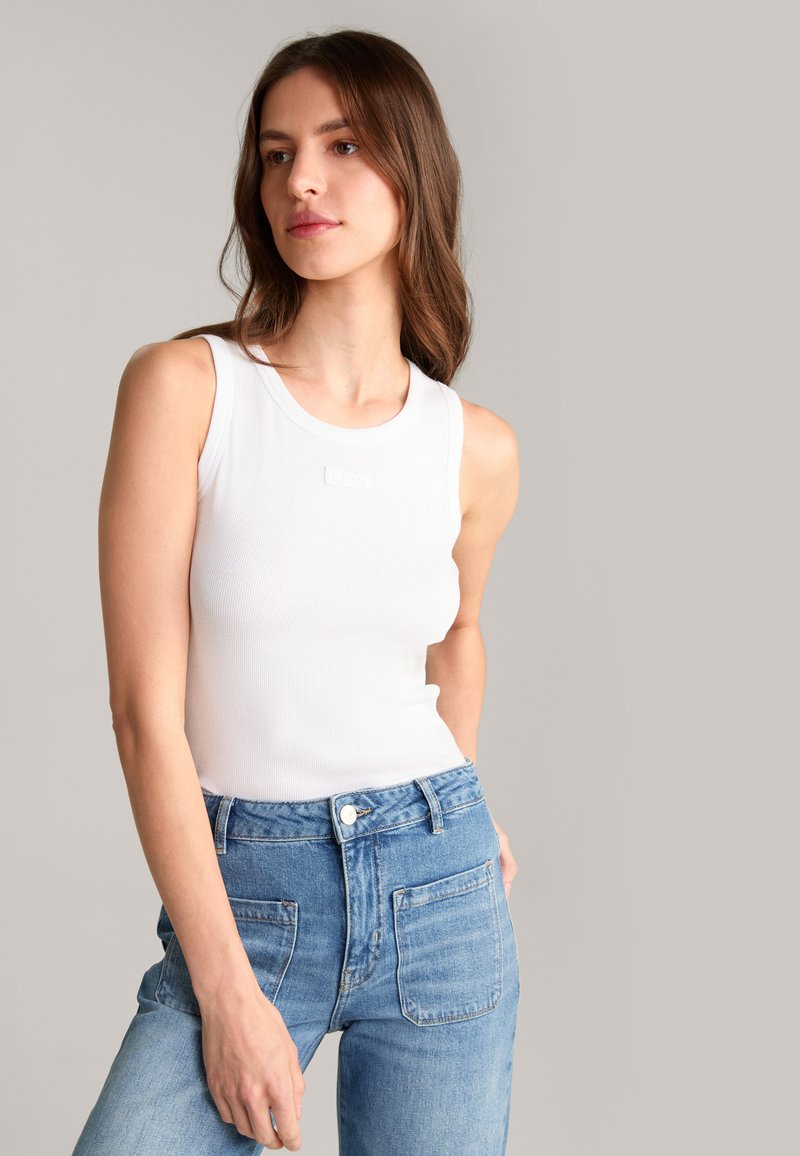Top in cotone bianco a costine con scollatura tonda, caratterizzato da un piccolo dettaglio con logo, abbinato a jeans in denim blu a vita alta.