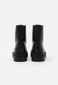 Botines de cuero negro hasta el tobillo con un acabado suave, puntera redonda y suela de goma gruesa y texturizada. Presentan costuras visibles en la parte trasera.
