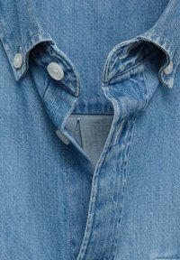 Ljusblå denimskjorta med krage, prydd med vita knappar och en fickkontur. Strukturerad tyg med subtila vertikala ränder.