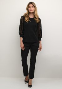 Black blouse with lace puff sleeves, paired with slim black trousers and black heels featuring silver accents. Smooth fabric with a fitted design.