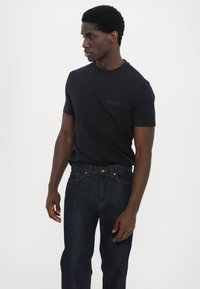 Svart bomull T-skjorte med korte ermer, med en liten logo på brystet, kombinert med mørke denimjeans og en gyllen knappdetalj.