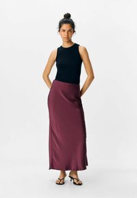 Top a righe nera abbinata a una lunga gonna di raso borgogna. La gonna si drappeggia in modo fluido e presenta una lucentezza delicata. Sandali neri con cinturini completano il look.