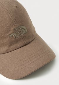 Barna baseball sapka, texturált szövetből készült, az elején hímzett logóval. Kerekített karimával és varrási vonalakkal rendelkezik.