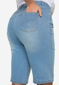 Pantaloni corti in denim azzurro chiaro con vestibilità rilassata, design a cinque tasche e dettagli di cucitura. Presentano una tasca sul retro con un contorno visibile.