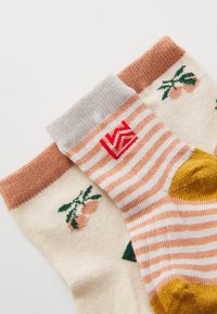 Due paia di calze: una crema con frutti arancioni e foglie verdi; l'altra a righe rosa e bianche con punta gialla e polsino grigio con logo.
