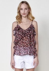 Top senza maniche con stampa floreale in nero, rosa e bianco. Tessuto trasparente con spalline sottili e regolabili. Abbinato a pantaloni corti bianchi.
