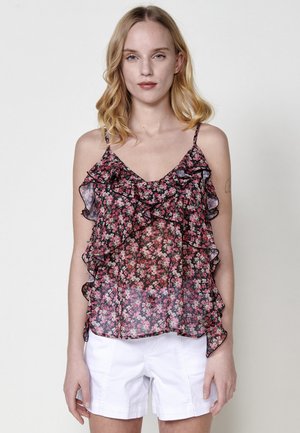 Top sans manches à imprimé floral avec volants en noir, rose et blanc. Tissu léger avec des bretelles ajustables fines. Associé à un short blanc.