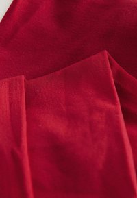 Red fabric with a soft texture, featuring smooth and ribbed sections, layered in a casual arrangement.