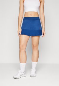 Saia desportiva azul com um design em camadas, feita de tecido leve. Apresenta um cós elástico e um pequeno detalhe de logotipo.