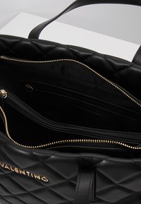 Borsa a tracolla in pelle nera trapuntata con zip in tonalità oro, multiple compartimenti e una superficie testurizzata. L'interno presenta una fodera in tessuto liscio.