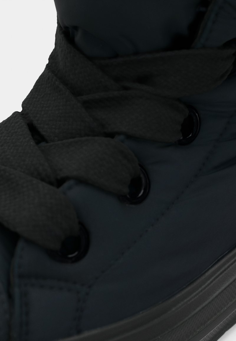 Sort højhælet støvle med en glat, polstret overdel, der har tykke snørebånd og runde huller, samt en struktureret gummisål.