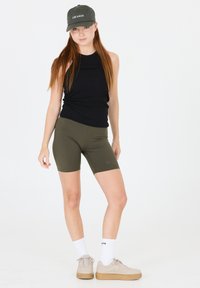 Top sans manches noir côtelé, shorts ajustés vert olive, baskets beige avec semelles tan, et chaussettes blanches mi-mollet. La casquette affiche le texte "LES ARGS".
