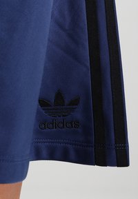 Marina blå Adidas-shorts i strukturerad tyg med svarta sidostråk och en svart broderad logotyp nära fållen.