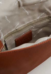 Interno di una borsa in pelle marrone con rivestimento beige chiaro e branding "Tamaris" ripetuto; include una tasca con zip per la conservazione.
