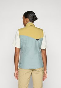 Le gilet léger présente une partie supérieure jaune, une partie inférieure bleue et un accent noir. Fabriqué en matériau lisse et résistant à l'eau.